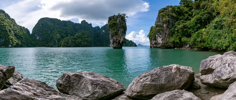 Limestone karst island rising from turquoise sea surrounded by jungle-covered cliffs in tropical bay
