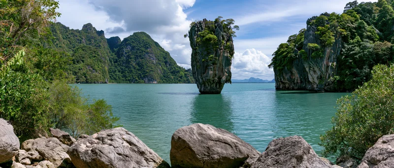 Limestone karst island rising from turquoise sea surrounded by tropical jungle cliffs in thailand