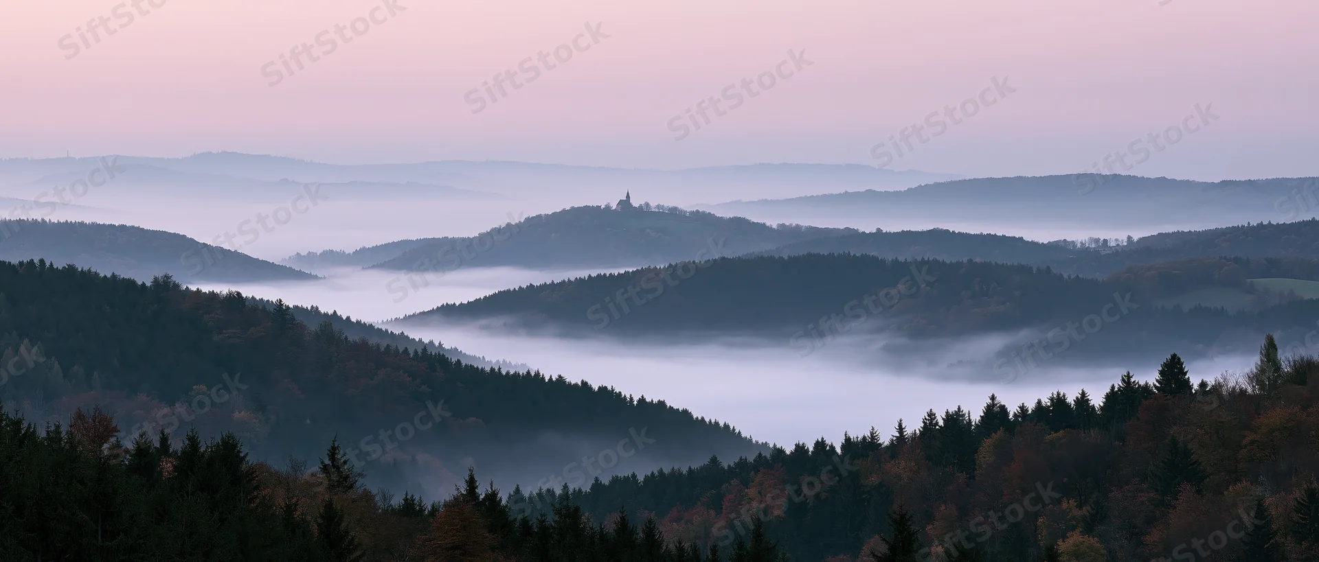 Misty valley surrounded by forested hills under pink dawn sky