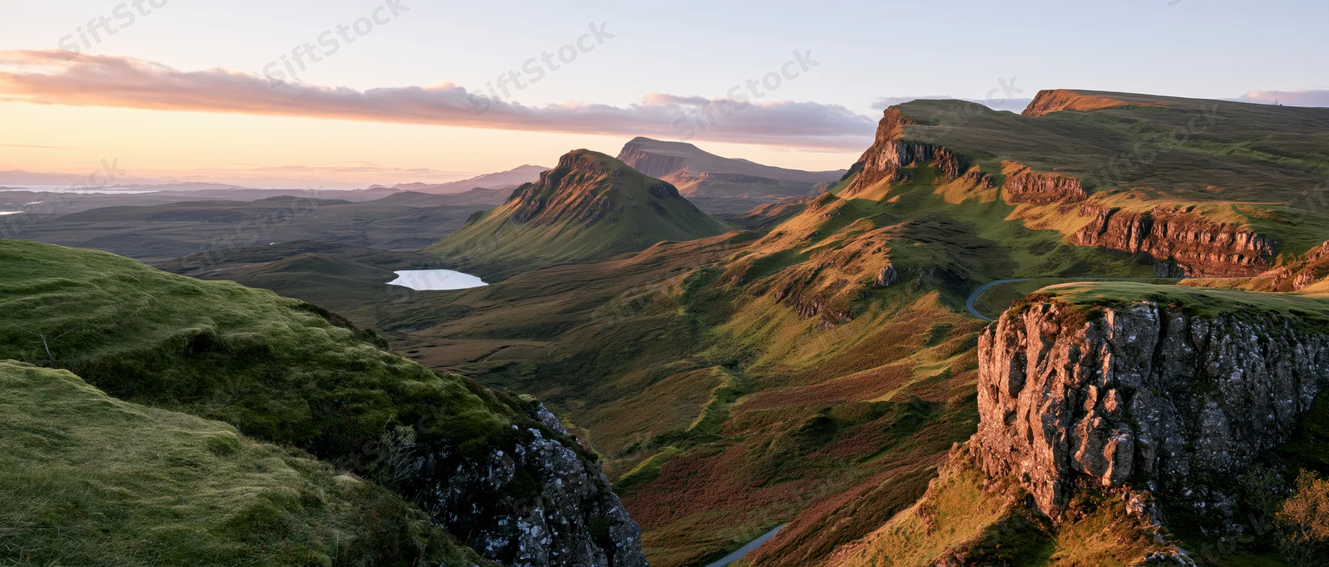 Rolling green hills and rocky cliffs in a mountain valley at sunset