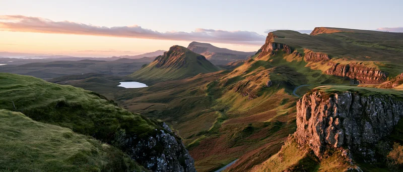 Rolling green hills and rocky cliffs in a mountain valley at sunset