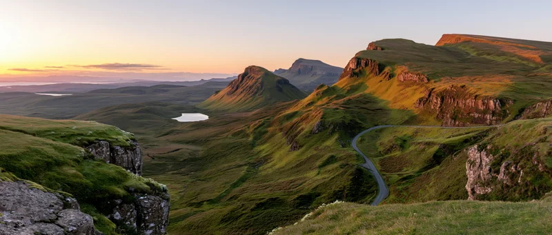 Winding road through green hills and valleys at sunset in the Scottish Highlands