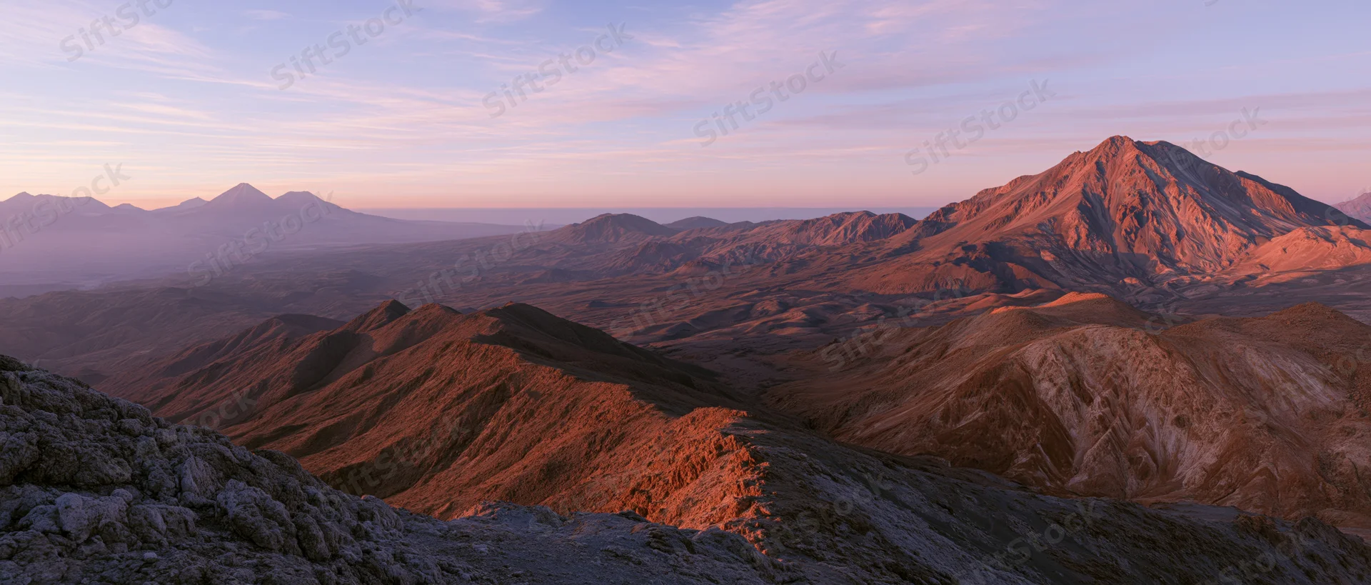 Rugged mountain peaks and valleys bathed in warm sunset light under a soft pastel sky
