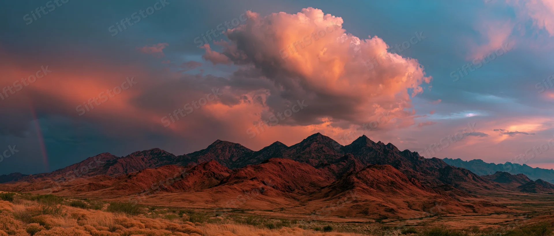 Rugged desert mountains under dramatic sunset clouds with stormy sky and rain in valley