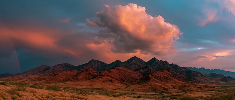 Rugged desert mountains under dramatic sunset clouds with stormy sky and rain in valley