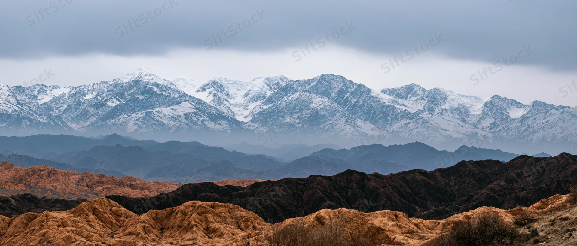 Snow-capped mountain range layered over arid desert canyons under overcast sky