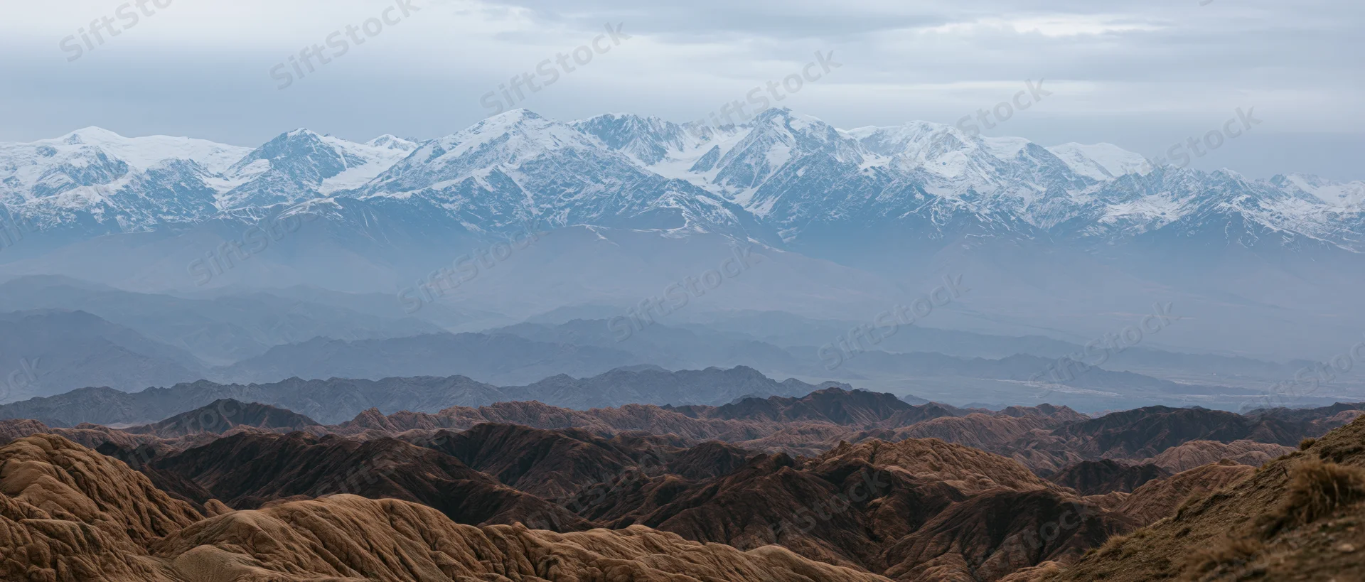 Snow-capped mountain range layered over arid desert terrain under hazy sky