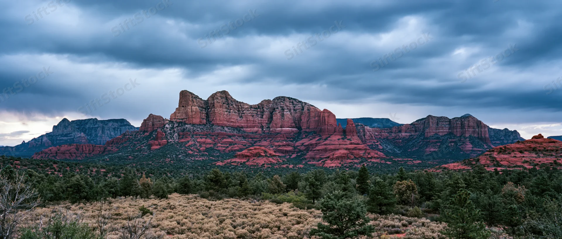 Red rock formations rise above desert scrubland under cloudy twilight sky