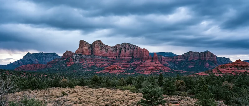 Red rock formations rise above desert scrubland under cloudy twilight sky