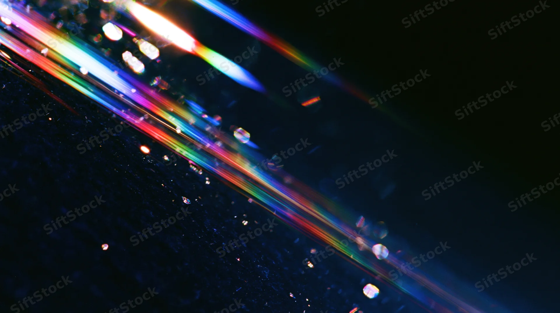 Colorful light streaks refracting across a dark surface with bokeh highlights