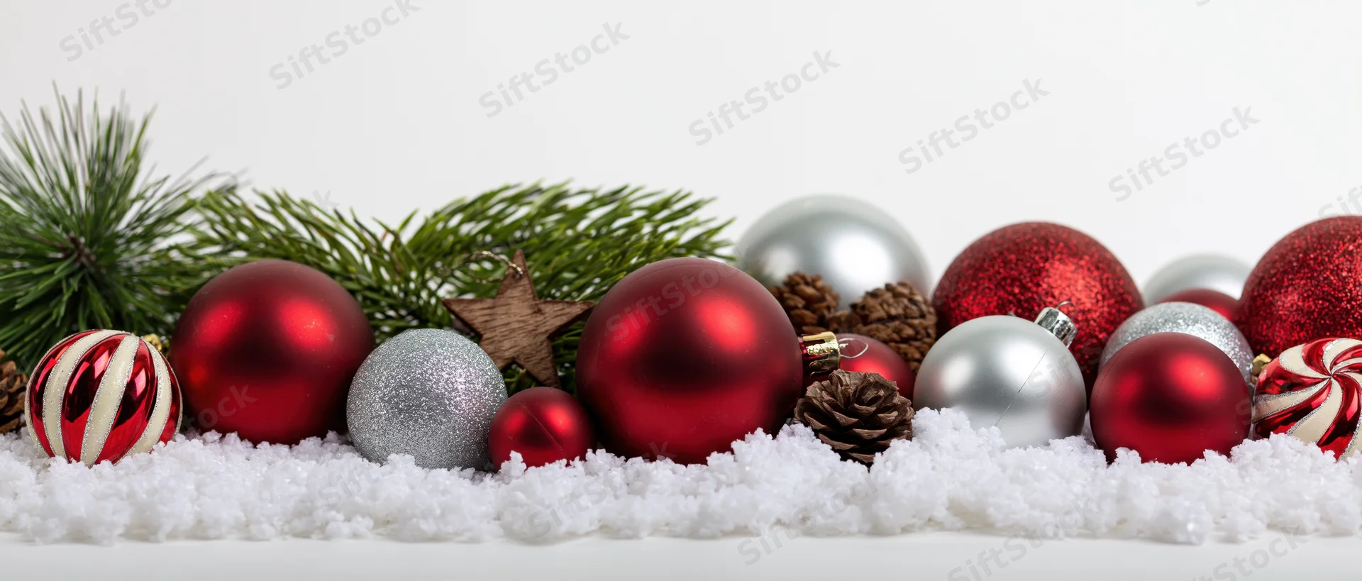 Christmas ornaments arranged with pine branches and pinecones on artificial snow against white background