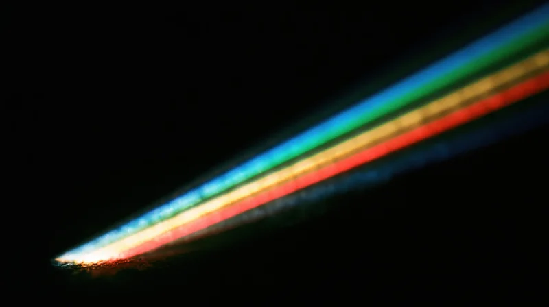 A diagonal rainbow light spectrum created by refraction in darkness