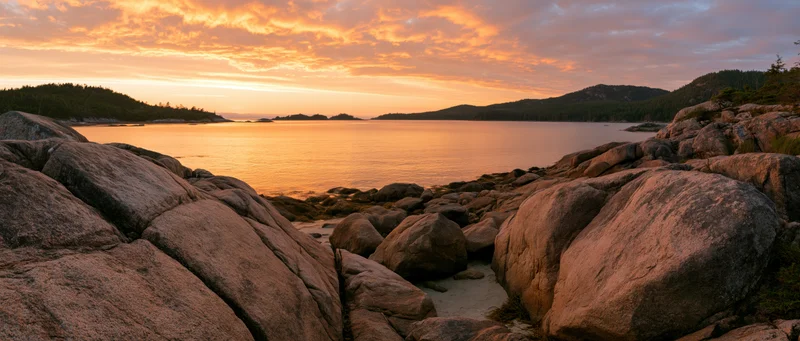 Rocky coastline at sunset with calm ocean and distant islands under golden sky