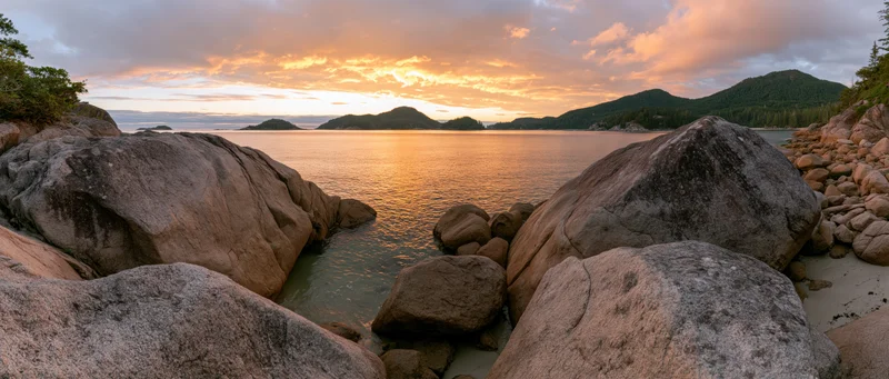 Rocky coastline at sunset with calm ocean and distant mountains