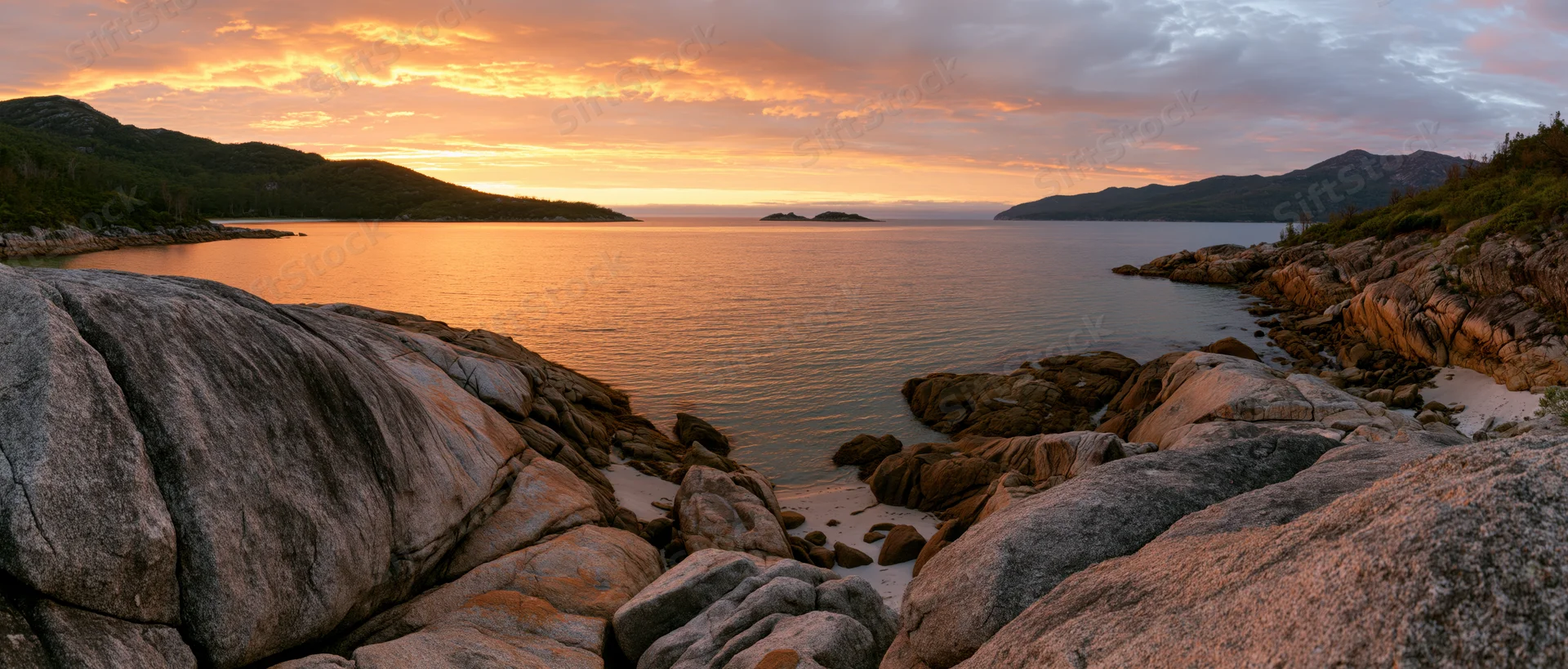 Rocky coastline at sunset with calm ocean and distant mountains