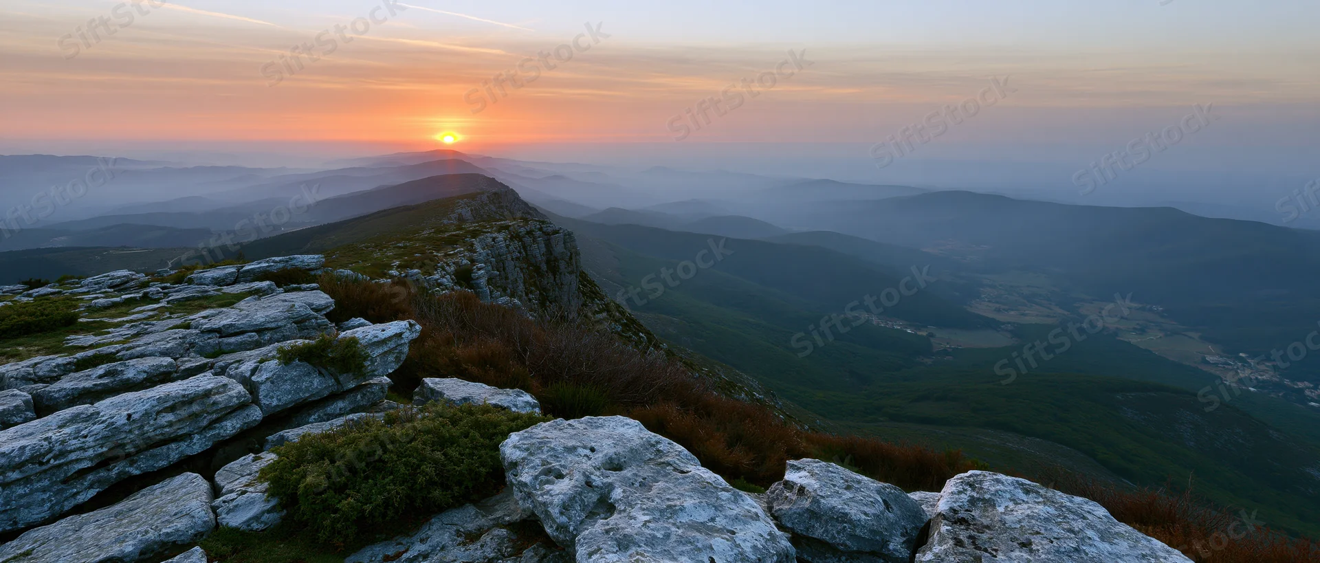 Sunrise over mountain ridge with rocky foreground overlooking misty valley