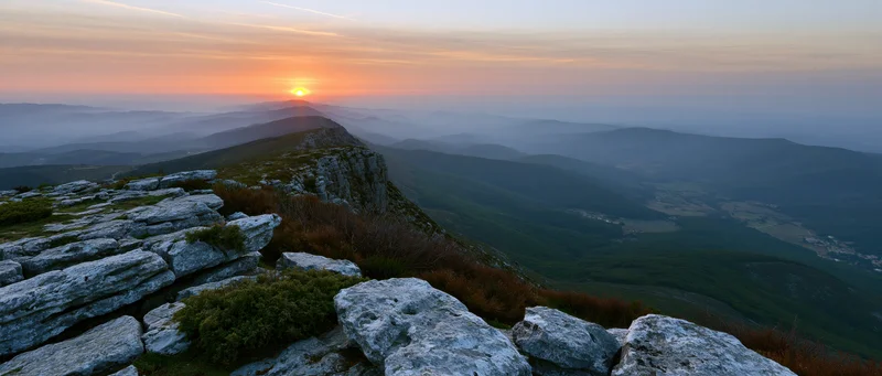 Sunrise over mountain ridge with rocky foreground overlooking misty valley