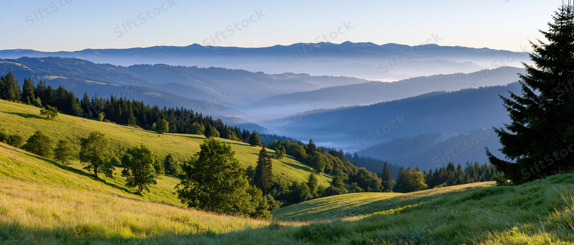 Rolling green hills and forested valleys under morning light with distant mountain ranges in soft mist
