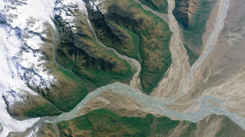 Braided river flowing through mountain valley with snow-covered peaks and green slopes