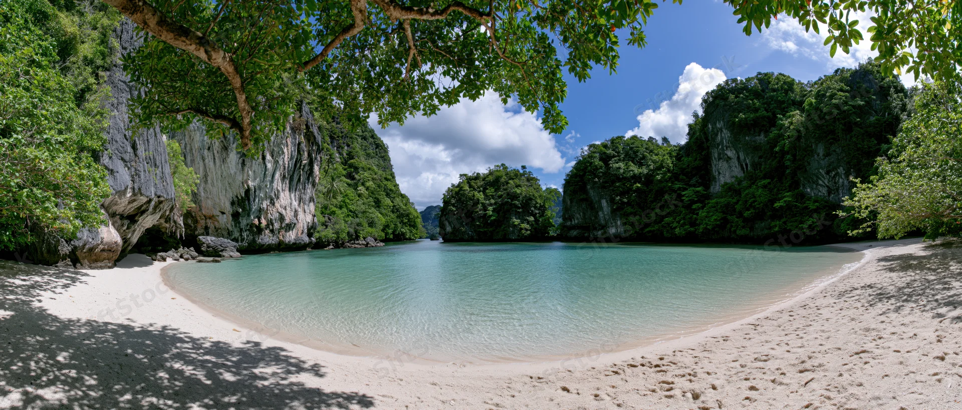 Tranquil tropical beach with turquoise lagoon surrounded by lush jungle cliffs under a blue sky