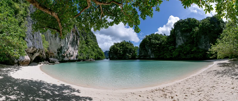 Tranquil tropical beach with turquoise lagoon surrounded by lush jungle cliffs under a blue sky