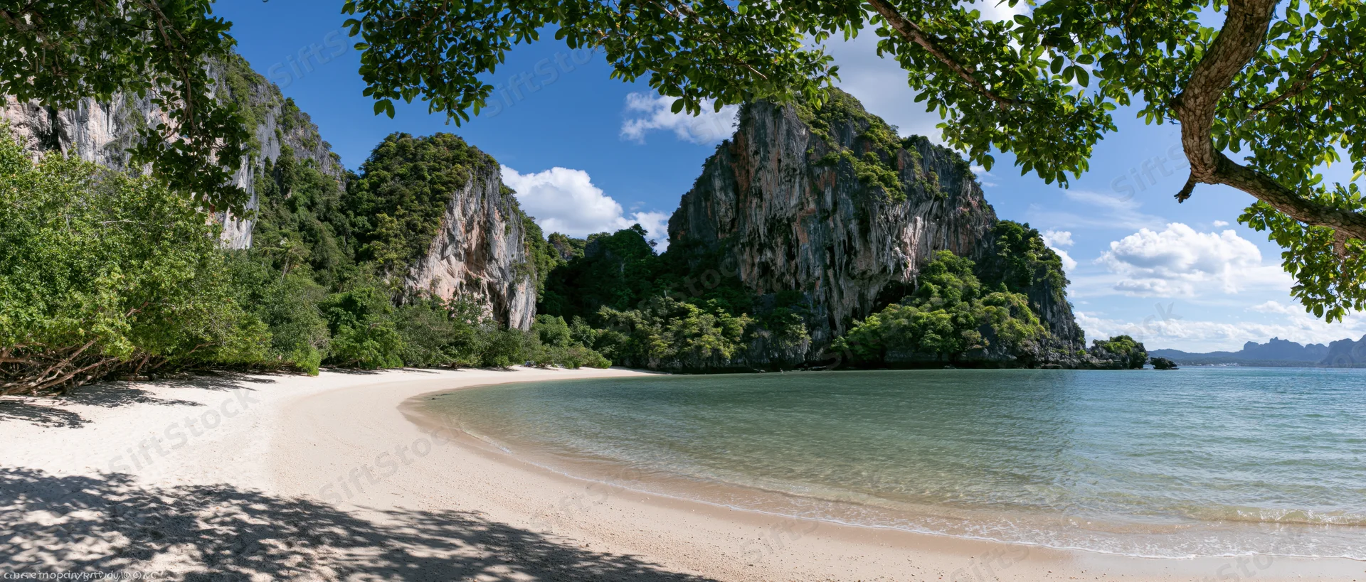 Sandy beach curving along a calm ocean with limestone cliffs and jungle under a blue sky