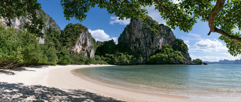 Sandy beach curving along a calm ocean with limestone cliffs and jungle under a blue sky