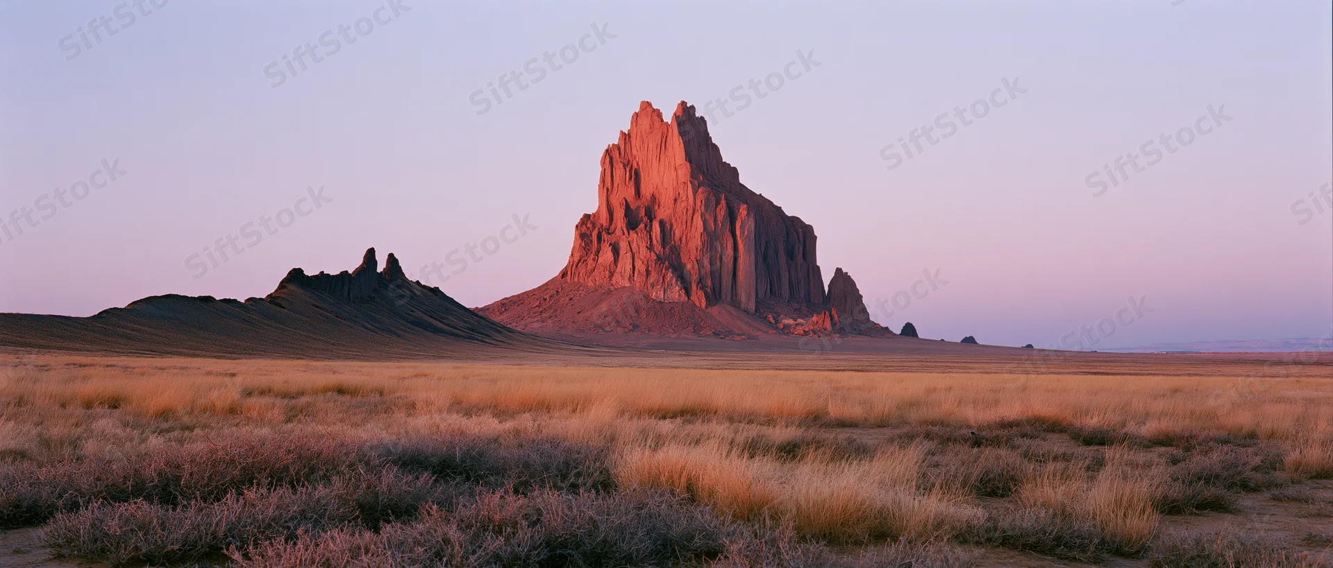 Red sandstone butte rising from arid desert plain at twilight