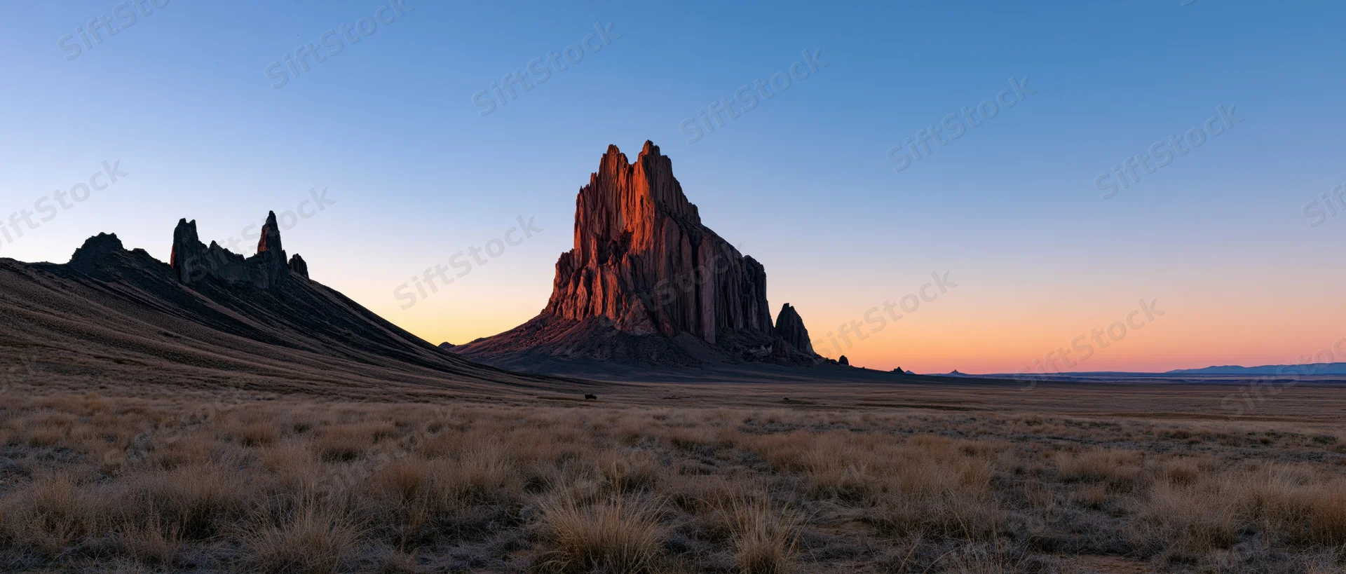 Large rock formation rising from desert plain at sunset