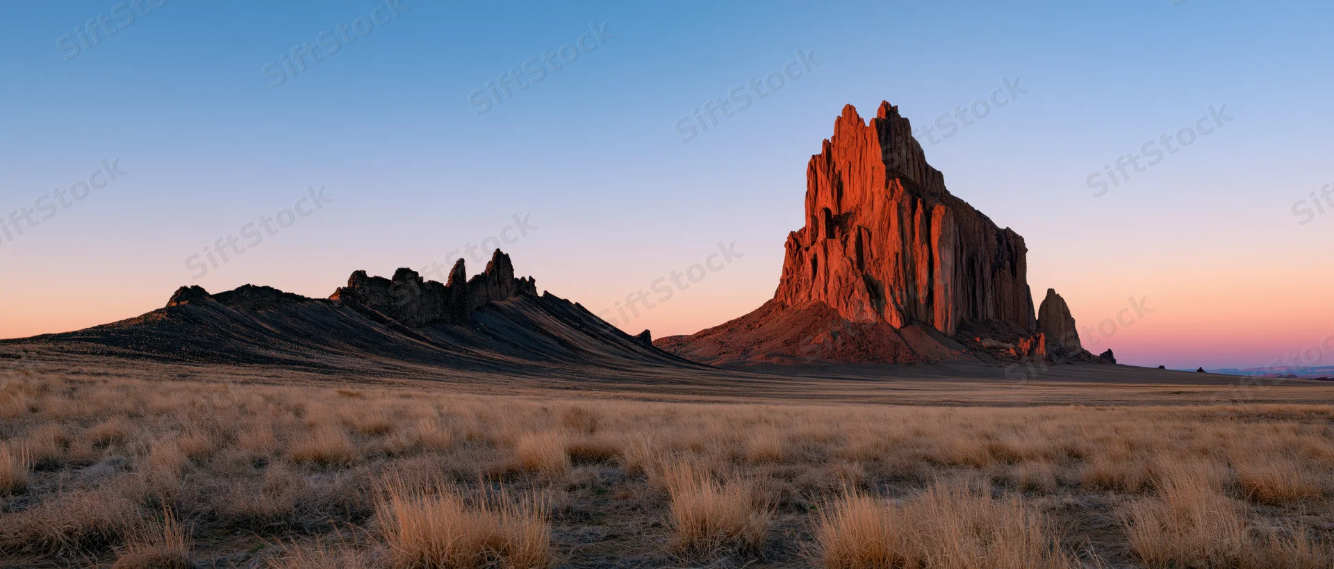 Red rock formation rising from desert plain at sunset