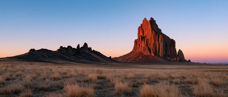 Red rock formation rising from desert plain at sunset