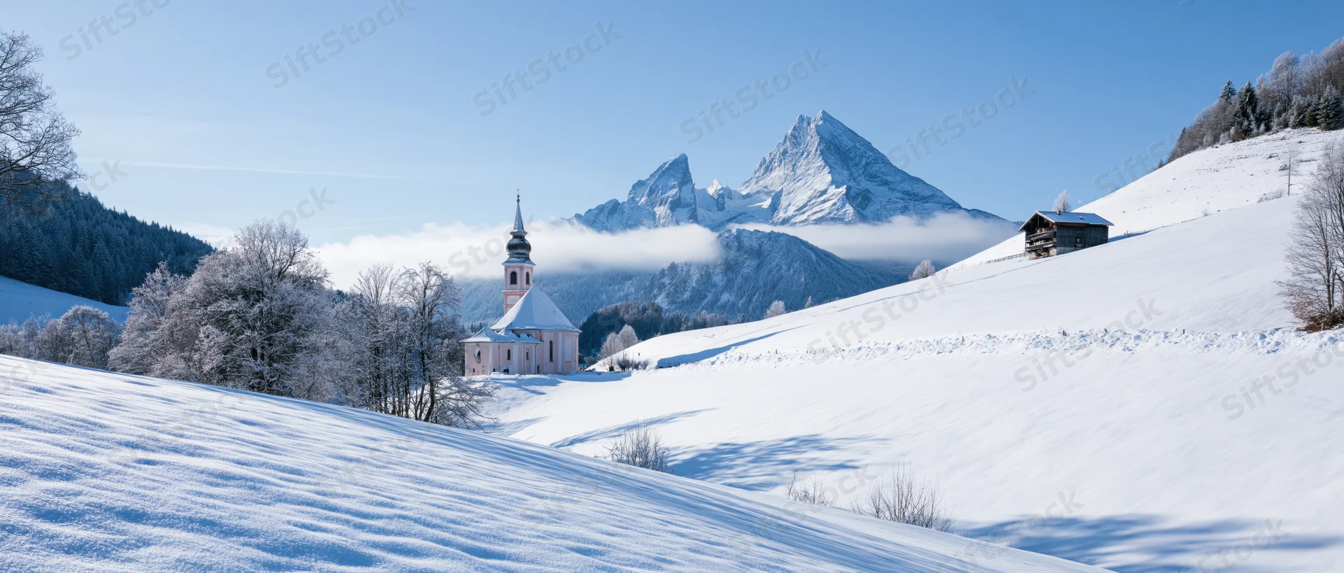 Snow-covered alpine church on a hillside with mountains in the background