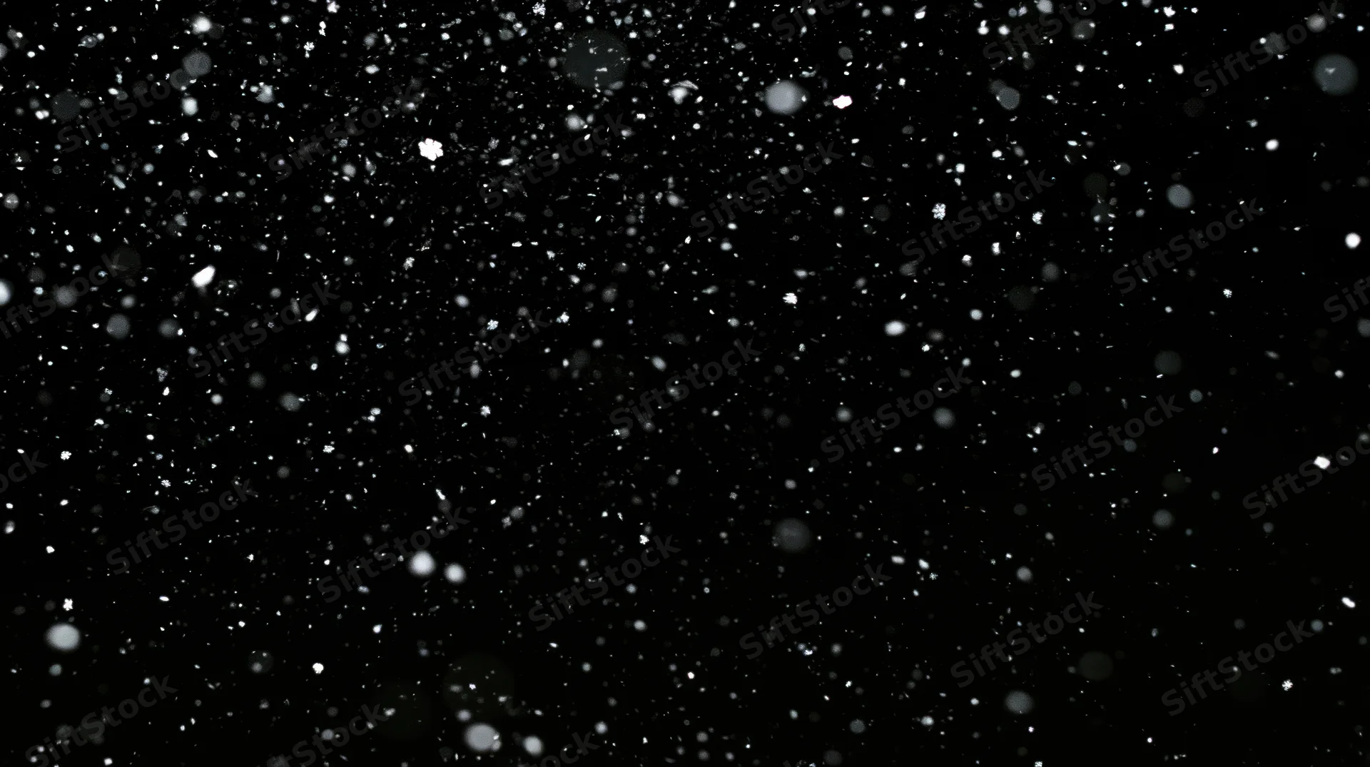 Snowflakes falling against a black background in a winter night scene