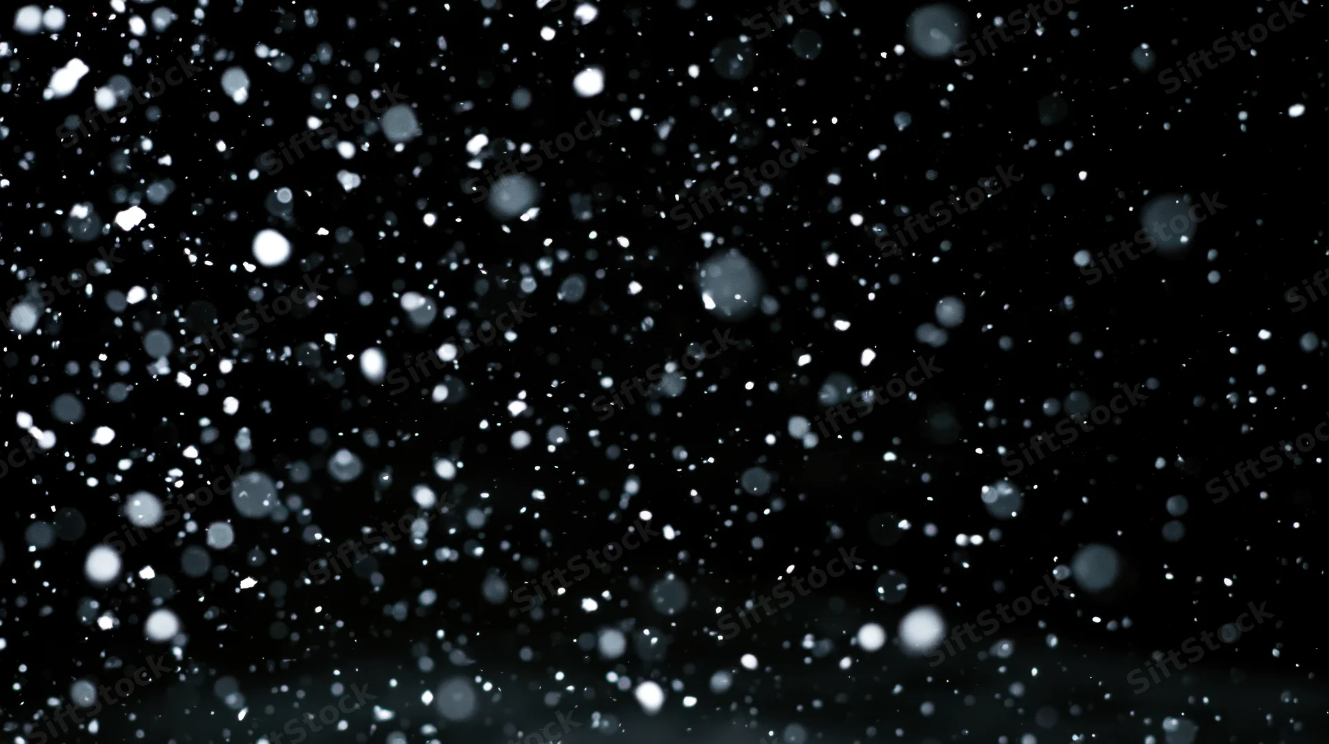 Snow falling against a dark night sky with bokeh highlights and soft focus