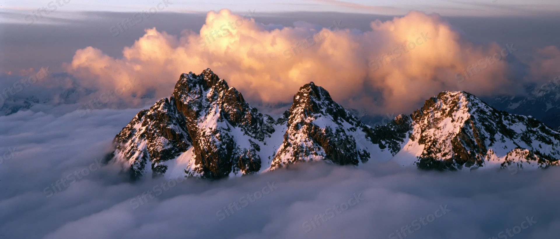 Snow-covered mountain peaks rising above a sea of clouds at sunrise