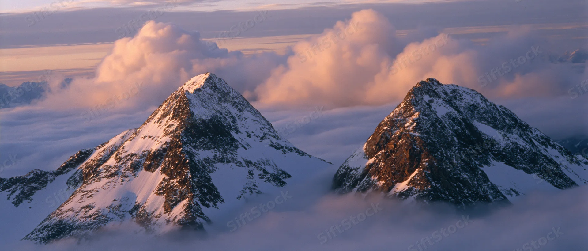 Snow-covered mountain peaks rising above a sea of clouds at sunrise