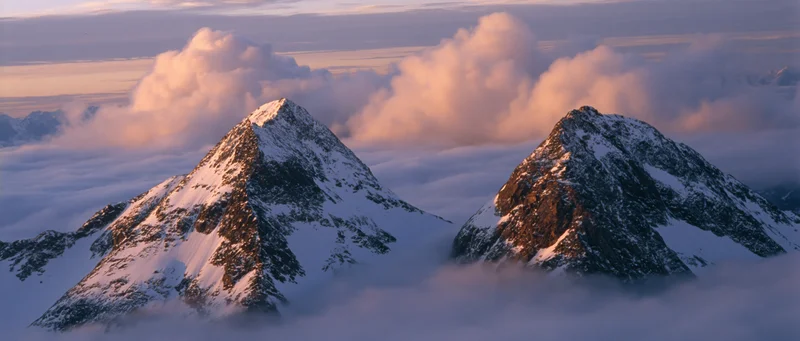 Snow-covered mountain peaks rising above a sea of clouds at sunrise