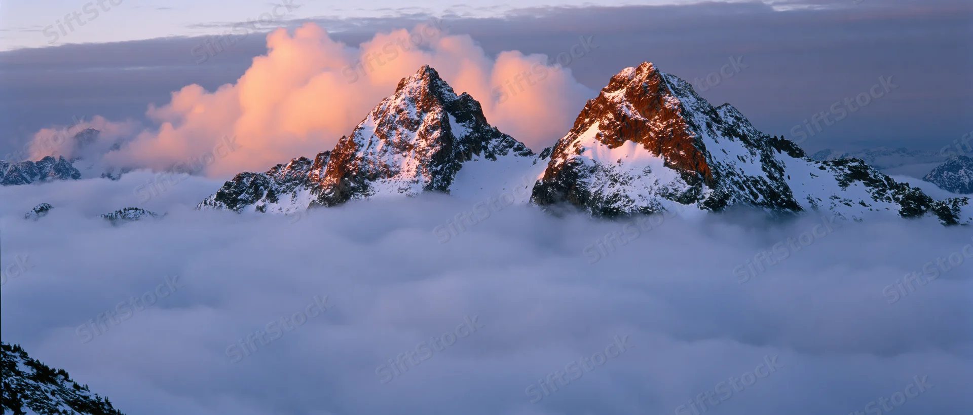 Snow-covered mountain peaks rising above a sea of clouds at sunrise