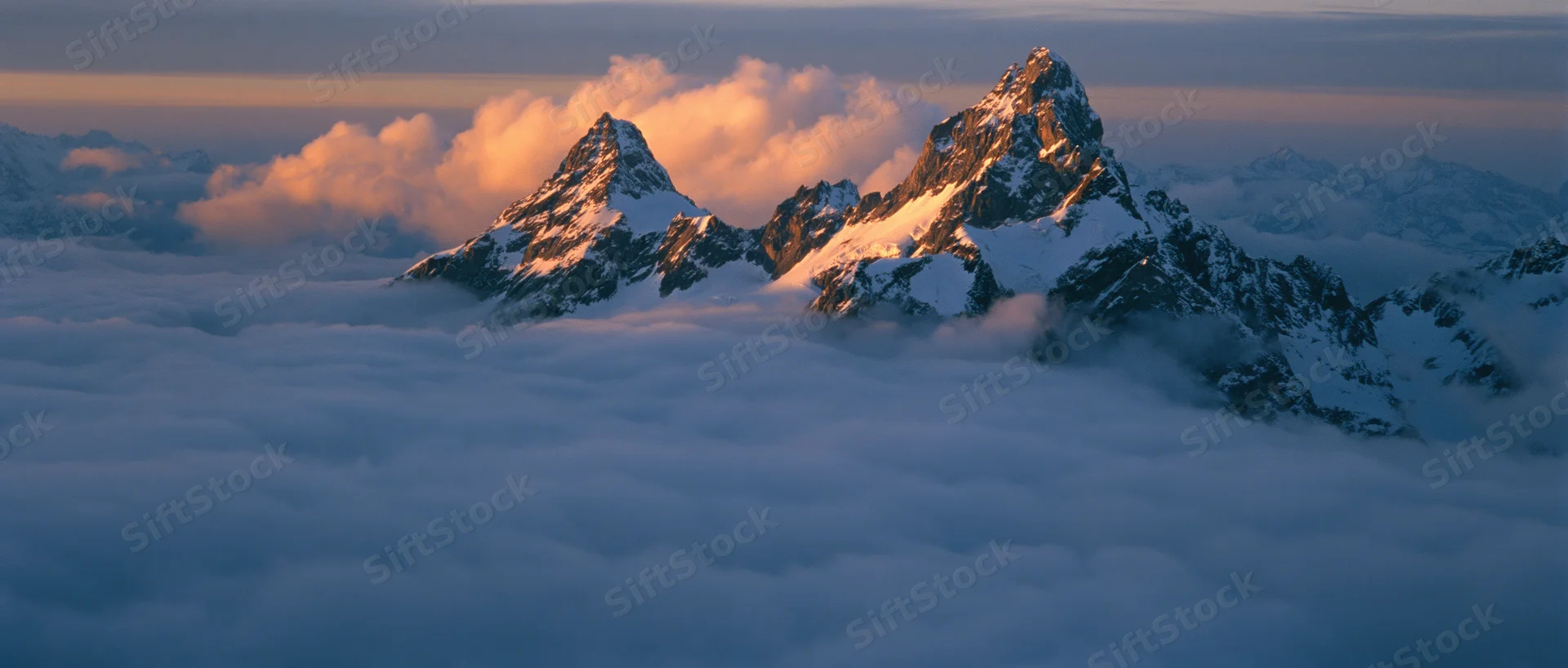 Snow-covered mountain peaks rising above a sea of clouds at sunrise