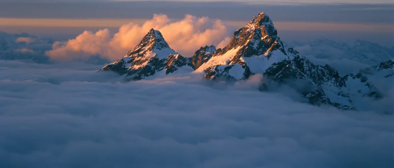Snow-covered mountain peaks rising above a sea of clouds at sunrise