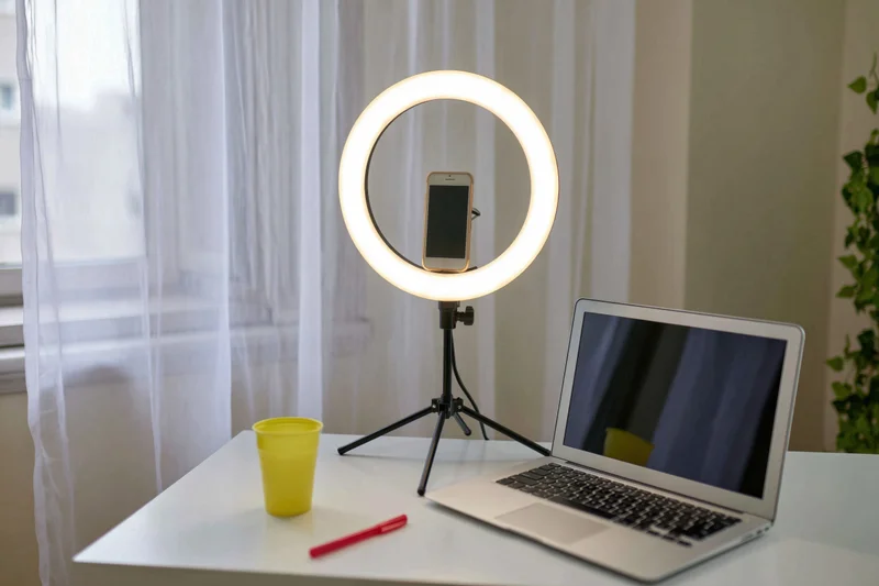 Laptop and ringlight setup on a desk with smartphone mounted for video recording in a home office