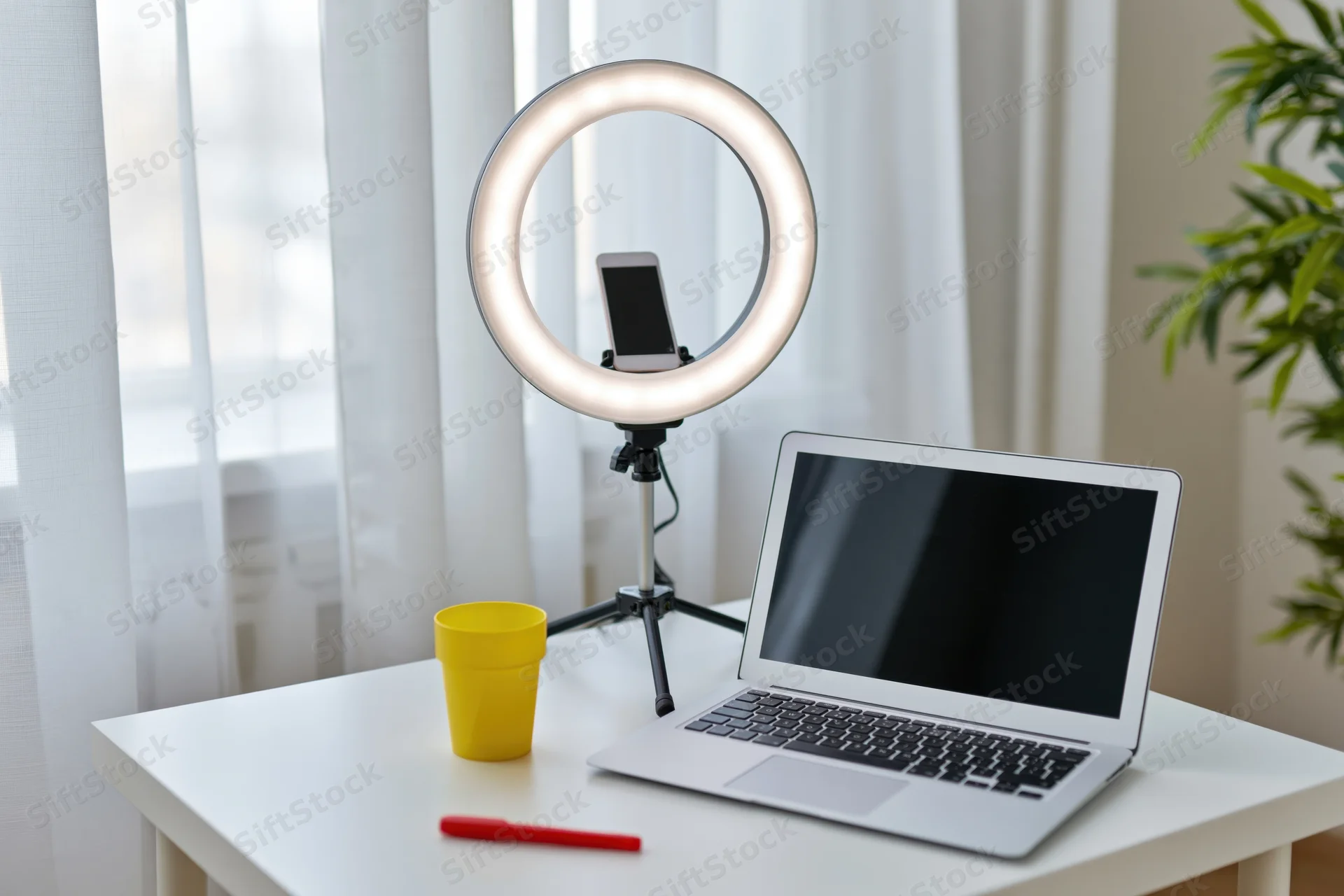 Laptop and ringlight setup on a white desk with smartphone, cup and pen for home content creation