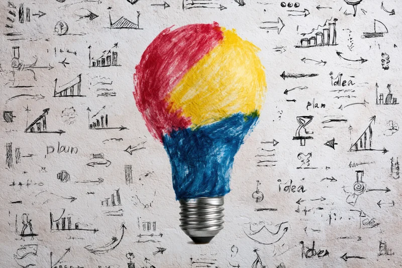 A hand-drawn lightbulb colored red yellow and blue on textured paper surrounded by sketches of graphs arrows and words like idea and plan
