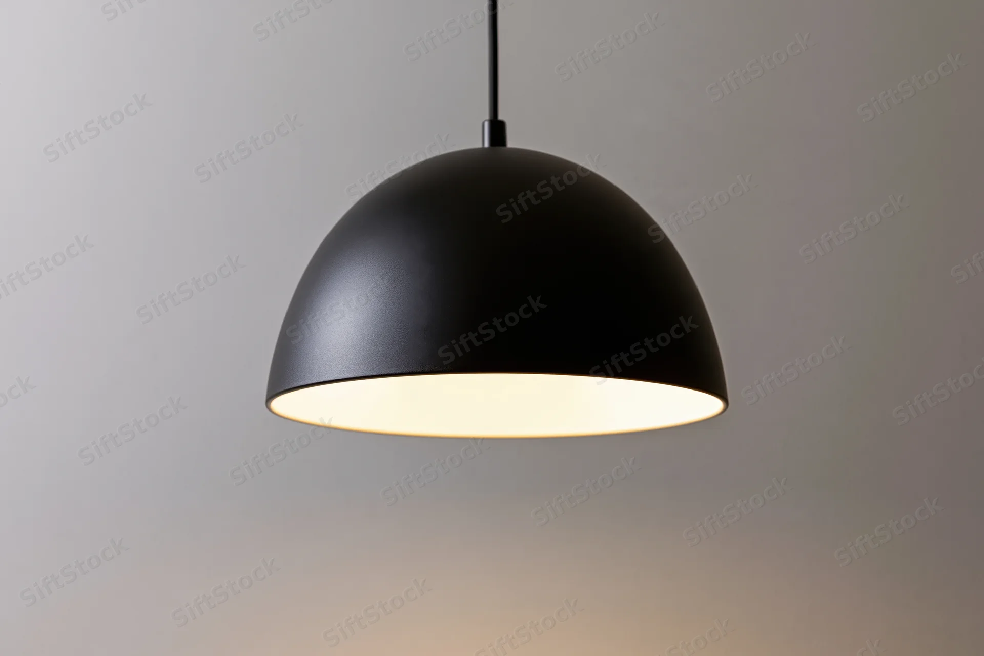 Matte black dome pendant lamp hanging from ceiling with warm glow against neutral background