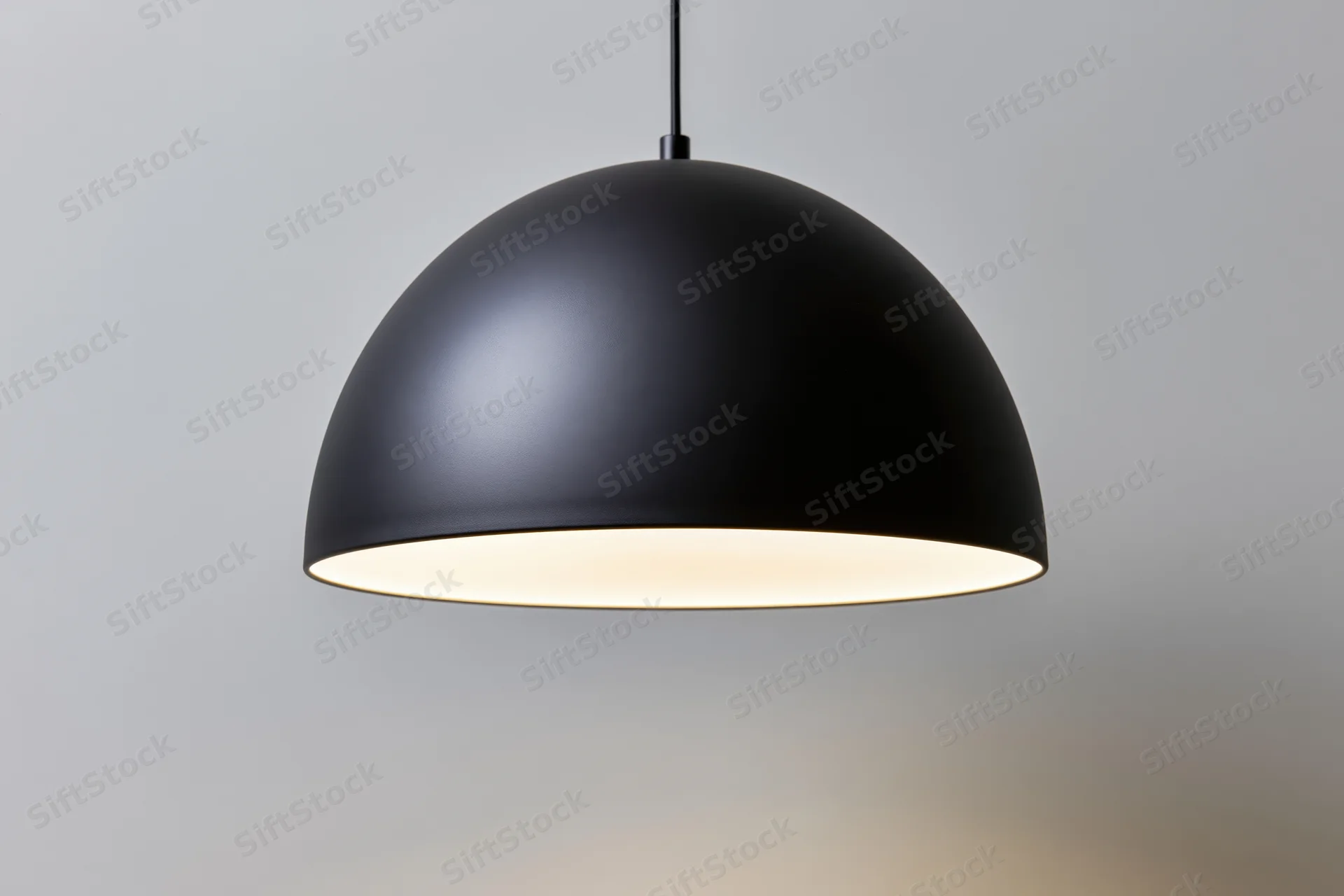 Matte black dome pendant lamp hanging from ceiling with warm glow against plain background