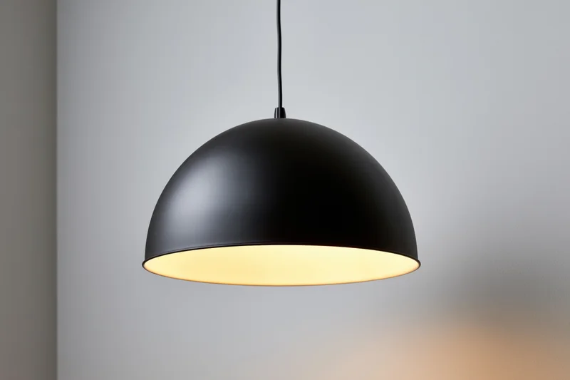 Matte black dome pendant lamp hanging from ceiling in minimalist interior with warm glow