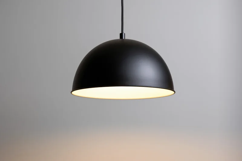 Matte black dome pendant lamp hanging from ceiling with warm glow against neutral background