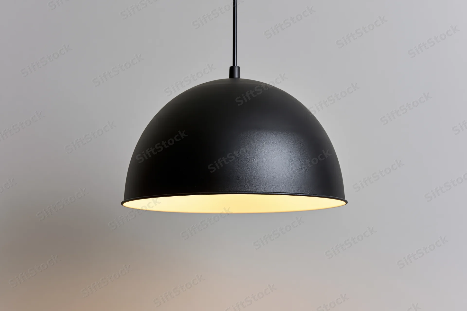 Matte black dome pendant lamp hanging from ceiling with warm glow against plain background