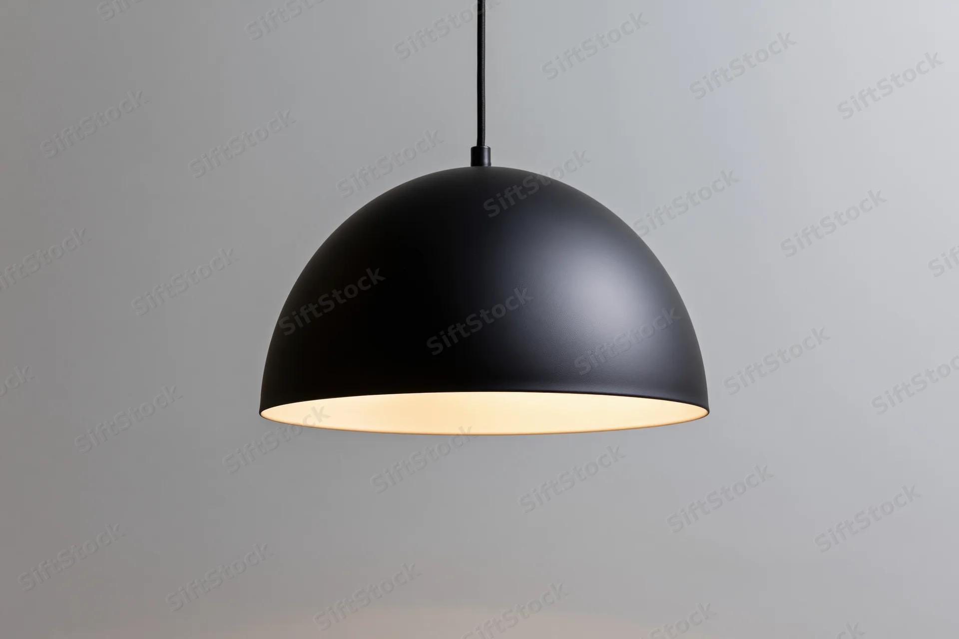 Matte black dome pendant lamp hanging from ceiling with warm glow against plain background