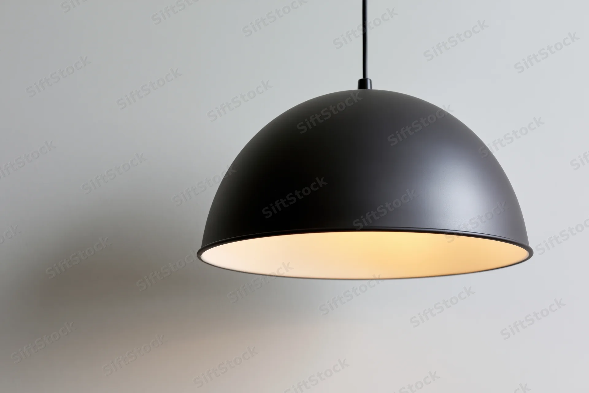 Matte black dome pendant lamp hanging from ceiling with warm glow against plain wall